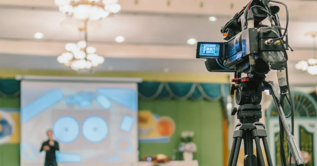 Kamera wideo na statywie nagrywa wystąpienie prelegenta na konferencji – nagrania udostępnione w serwisie YouTube
