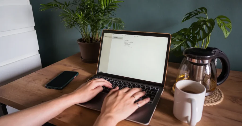 Osoba pracuje na laptopie przy drewnianym biurku z roślinami – uruchomienie strony internetowej konferencji
